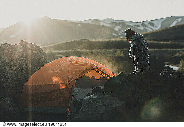 woman prepares tent for sleeping at sunset at campsite