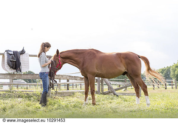 Woman preparing horse for horseback riding in rural pasture