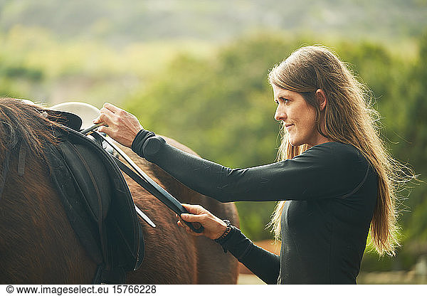 Woman preparing saddle for horseback riding