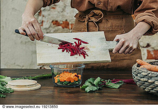 Woman preparing salad on table in front of wall