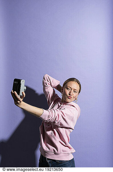 Woman puckering and photographing herself through camera against purple background