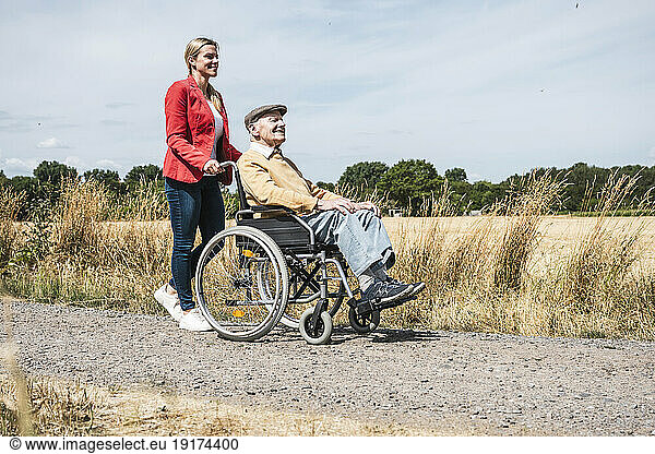 Woman pushing elderly man sitting in wheelchair by field