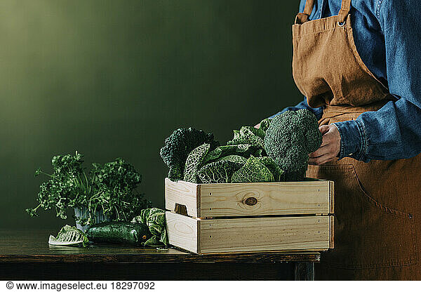 Woman putting fresh green vegetable in crate