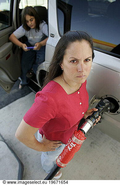 Woman putting gas in SUV with child in background.