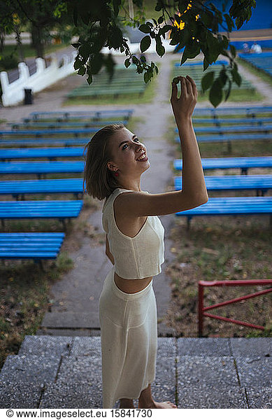 woman reaches for tree leaves smiling