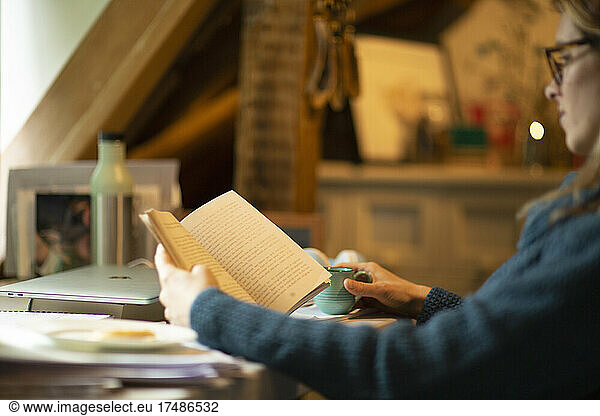 Woman reading book at desk in home office