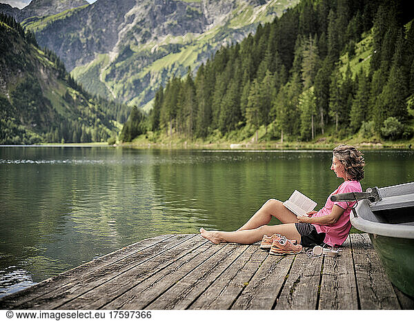 Woman reading book by rowboat at lake