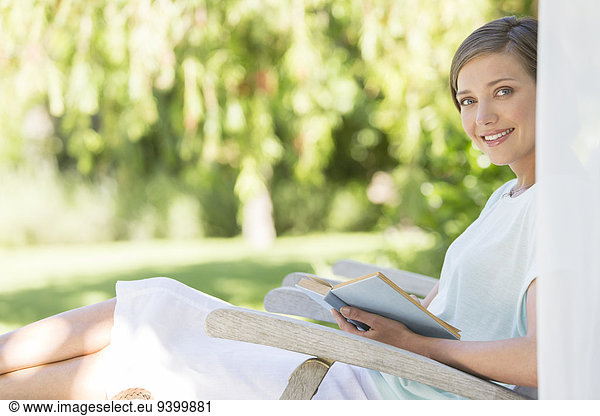 Woman reading book in lawn chair outdoors
