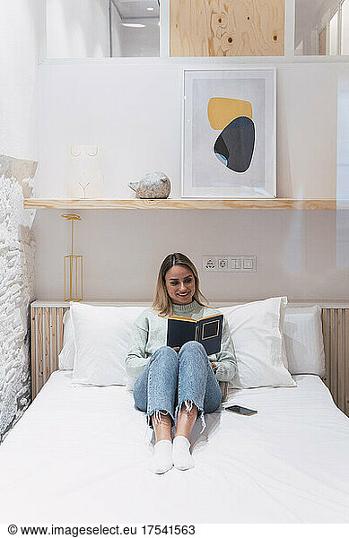 Woman reading book on bed at home