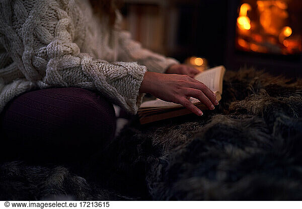 Woman reading book on blanket at cozy fireside