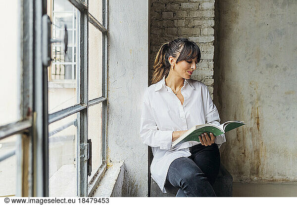 Woman reading book sitting by window