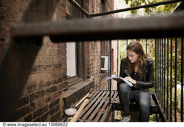 Woman reading book while sitting at fire escape
