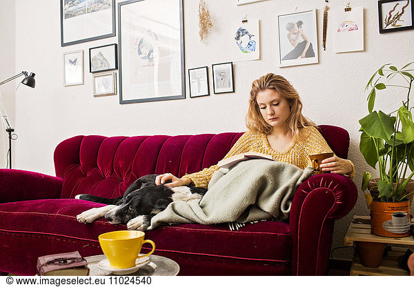 Woman reading book while sitting with dog on sofa at home