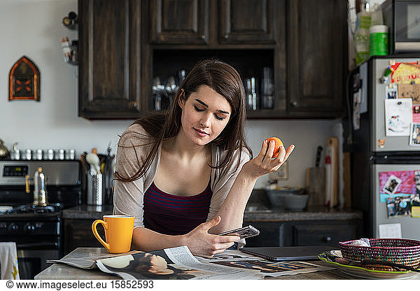 Woman reading newspaper while having breakfast at table in kitchen