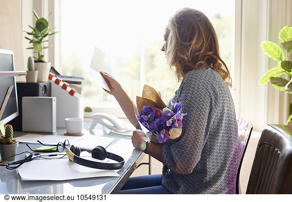 Woman receiving flower bouquet and reading card in home office