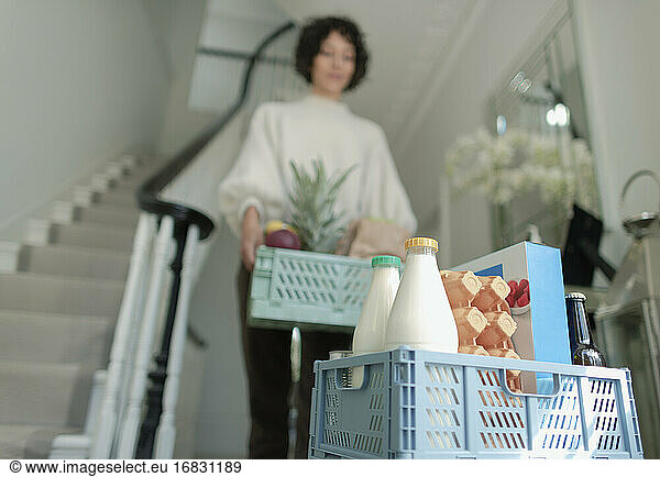 Woman receiving grocery delivery crates in foyer