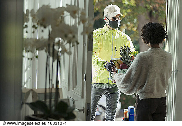 Woman receiving grocery delivery from courier in face mask at door