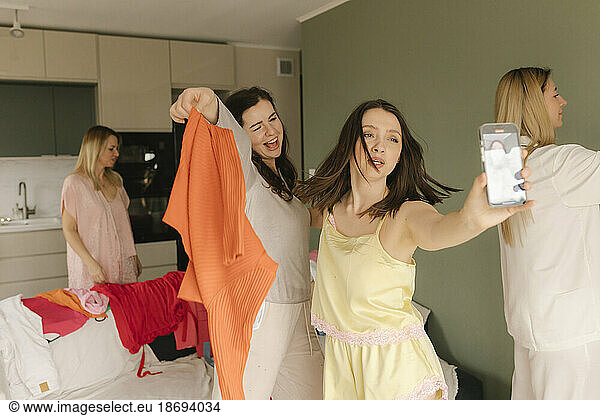 Woman recording friend through smart phone holding dress at home