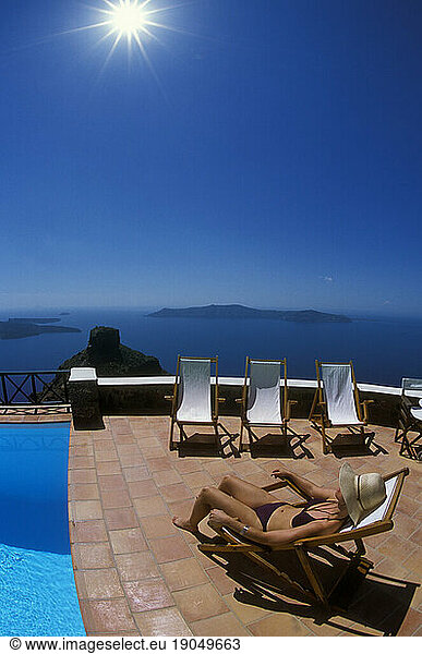 Woman relaxes poolside looking over the Caldera of Santorini  Greece.