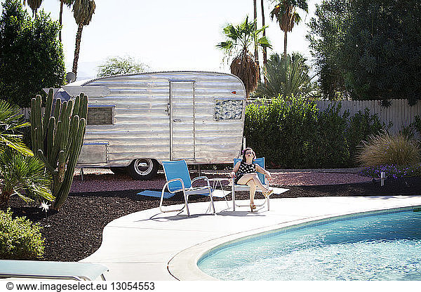 Woman relaxing on chair at poolside against camper van