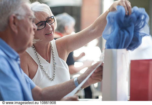 Woman removing scarf from shopping bag at sidewalk cafe