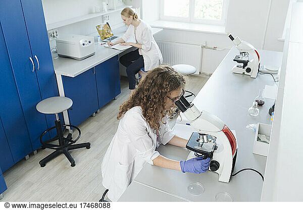 Woman researching through microscope in laboratory