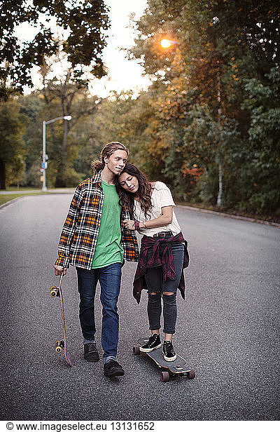 Woman resting head on man's shoulder while standing on skateboard