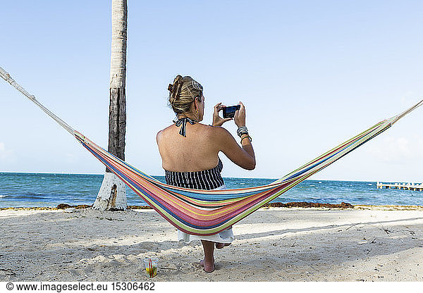 Woman resting in hammock taking picture with smart phone