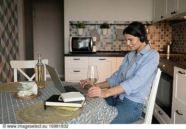 Woman resting in kitchen and browsing internet on laptop