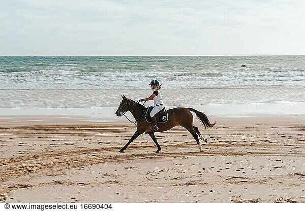 Woman riding Andalusian horse along beach in Spain