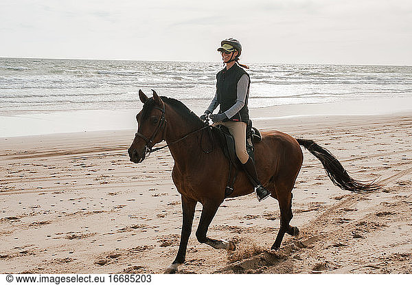 Woman riding Andalusian horse on the beach and smiling