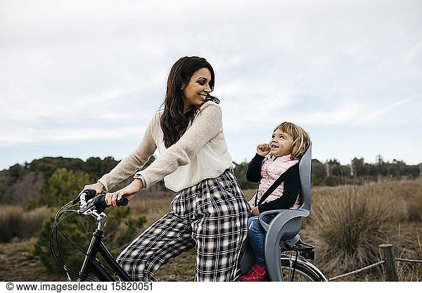 Woman riding bicycle in the countryside with daughter in child's seat