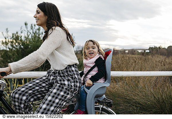 Woman riding bicycle in the countryside with happy daughter in child's seat