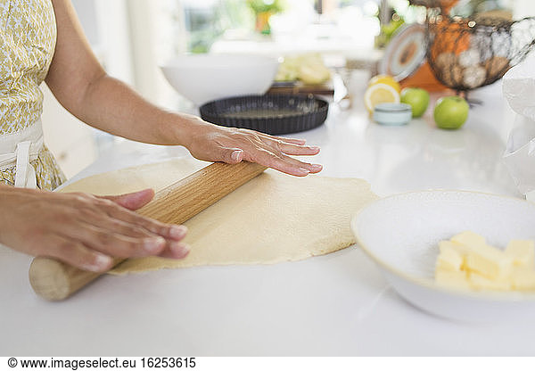 Woman rolling out pie dough with rolling pin on kitchen counter