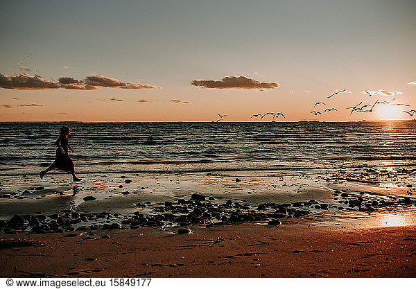 woman running on the beach in a dress with birds flying