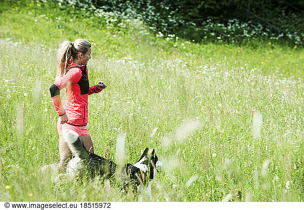 Woman running with dog in green field in sunny day