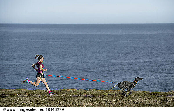 Woman running with dog on grass near sea