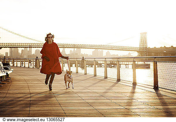 Woman running with dog on promenade against Williamsburg Bridge