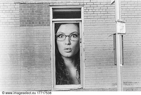 Woman's face visible peering out of a small window of a brick building; Winnipeg  Manitoba  Canada