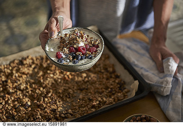 Woman's hand holding bowl of granola with yoghurt and berries
