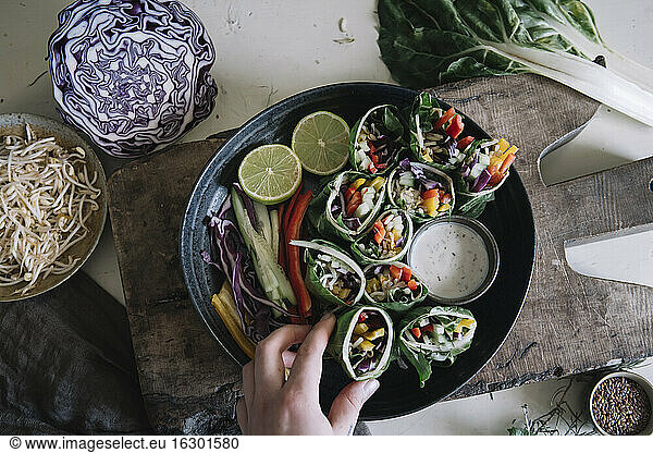 Woman's hand taking vegan roll with vegetables from bowl