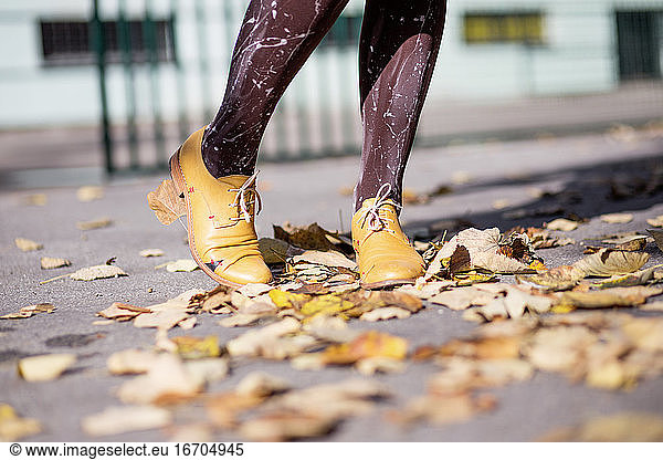 Woman's legs in yellow shoes on autumn leaves