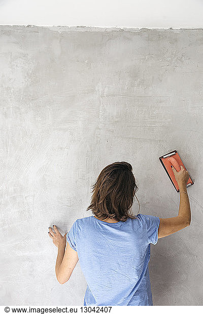 Woman sanding wall with hand sander during renovation