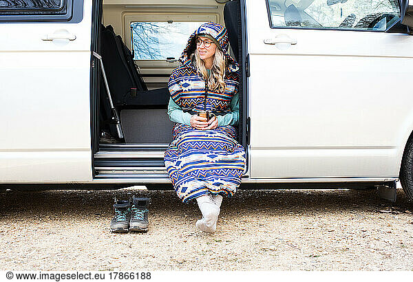 woman sat in a sleeping bag in a campervan on vacation
