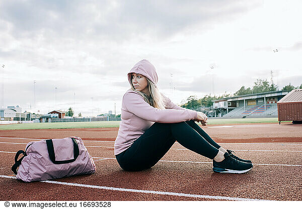 woman sat on a running track with a sports bag waiting