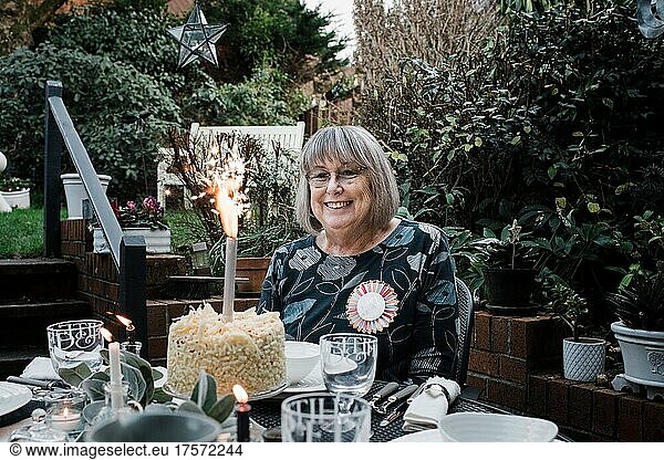 woman sat with a happy birthday badge and cake with sparklers