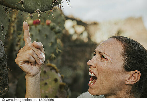Woman screaming in pain and touching cactus plant
