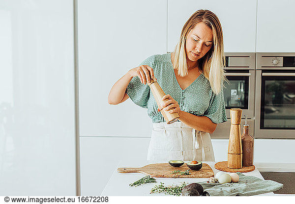 Woman seasoning avocado while standing at kitchen counter at home
