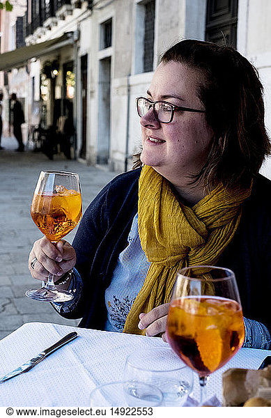 Woman seated at a table outdoors  holding a glass of Aperol Spritz
