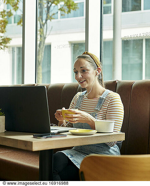 Woman seated in a cafe using a laptop interacting during an online call